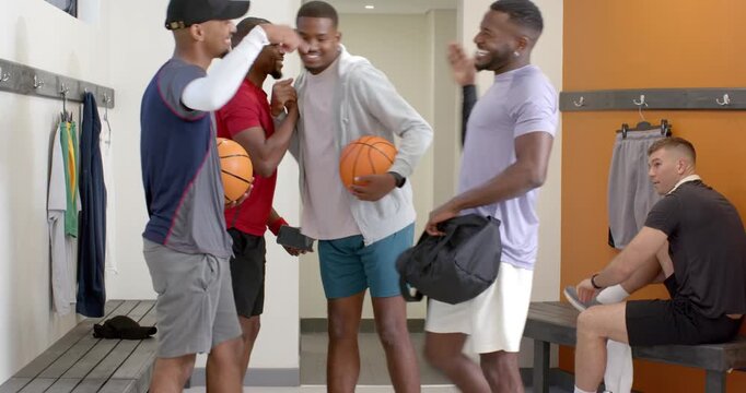 Diverse basketball teammates greeting newcomer on arrival, handshakes in locker room preparing