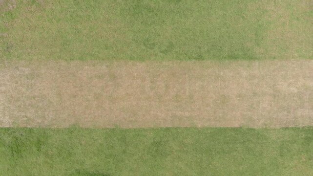 Camera pulling back revealing green brown pitch, stumps appearing left then right