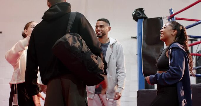 Diverse friends welcoming arriving teammate slinging duffel bag by boxing ring, chatting, laughing