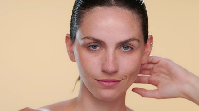 Headshot of fair-skinned bule-eyed beauty model confidently strokes her jawline presenting well hydrated skin on neutral background