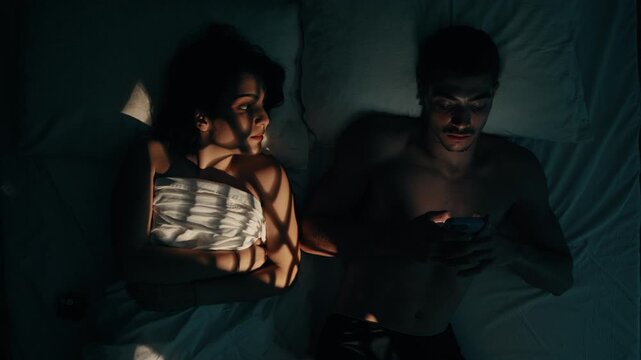 Married argue in bed at night because the man abuses his smartphone