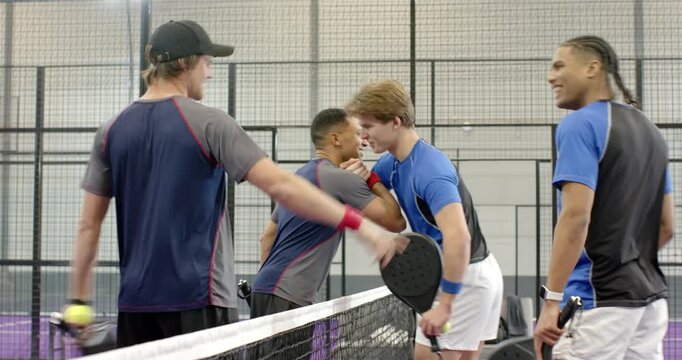 Four male players post-match shaking hands on court, grabbing paddles and exiting court