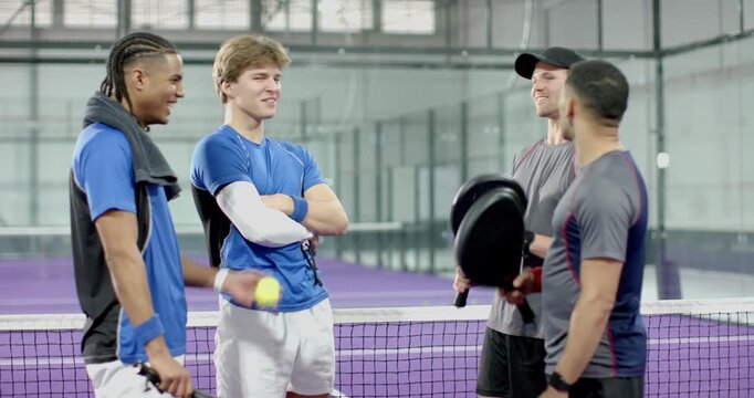 After greeting at padel net diverse male friends tossing ball with rackets, preparing for match