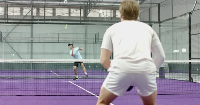 Male padel player responding to opponent drive, lunging volleying on court for fun