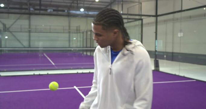 Male athlete dropping tennis ball, juggling with palm and paddle for control on purple court