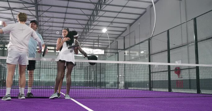 Diverse padel friends finishing match at net shaking hands, hugging, swapping rackets