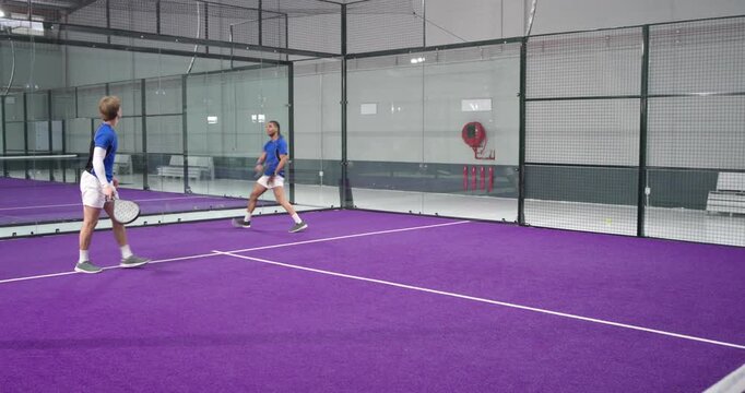 Ball rebounding off wall, starting padel rally diverse male teammates volleying ball