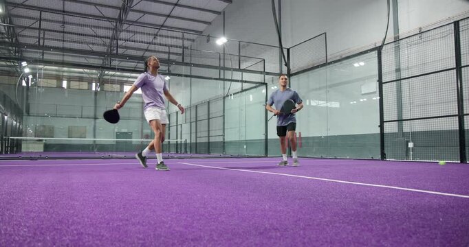 Following serve, diverse male athletes lunging and returning padel ball with rackets on court