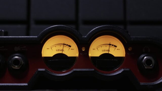 Close-up of backlit analog VU meters with needles measuring sound levels on an audio interface. Concept of sound engineering, music production, and precise audio measurement.