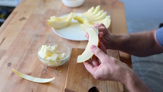 Man slicing ripe yellow melon into cubes on wooden table in home video Full HD kitchen