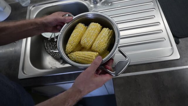 Boiled corn cobs cooling in pot under water at kitchen Full HD sink video