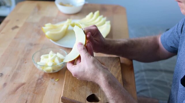 Man slicing ripe yellow melon into cubes on wooden table in home kitchen video Full HD