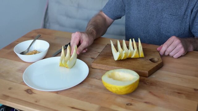 Man arranging sliced yellow melon wedges on white plate in kitchen video Full HD