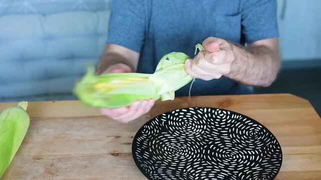 Man peeling fresh corn husk from cob during kitchen food preparation video Full HD