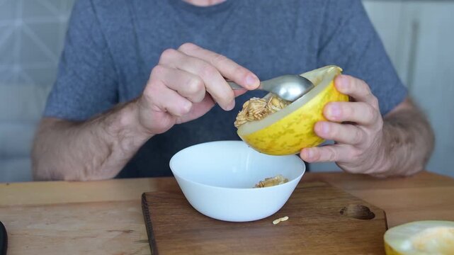 Man removing seeds from fresh yellow melon with spoon in home kitchen preparation video Full HD