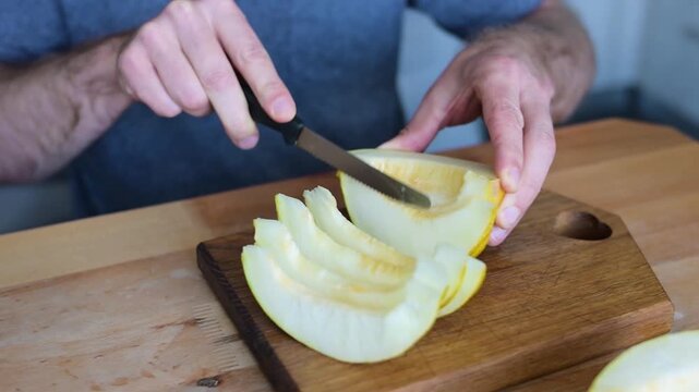 Man cutting yellow melon half with knife on wooden board in video Full HD kitchen