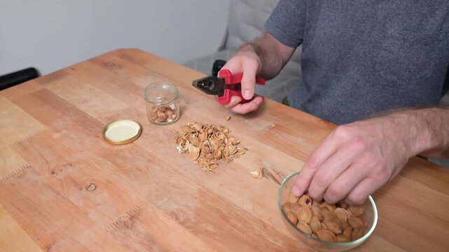 Man cracking apricot kernels with pliers at wooden kitchen table preparing healthy ingredients video Full HD