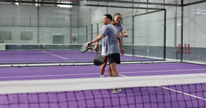 After winning rally two male teammates shaking hands pumping fists with rackets on court