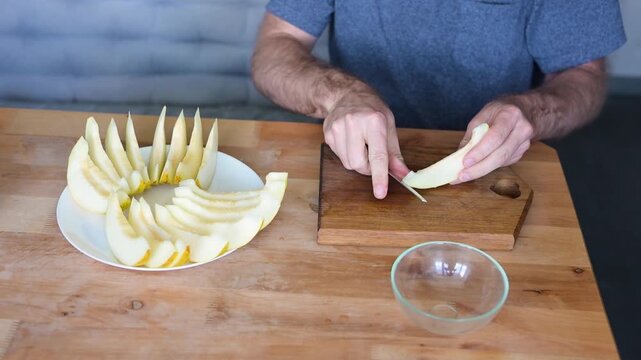 Man carving melon wedge and arranging fruit slices on white plate in kitchen video Full HD