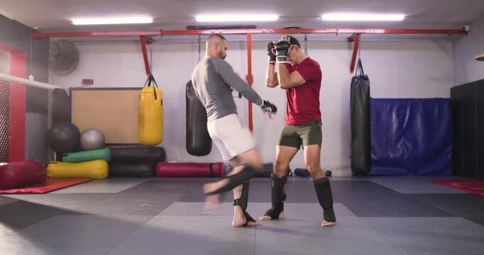 Stepping on mat, diverse male sparring partners exchanging jabs and kicks at gym for practice