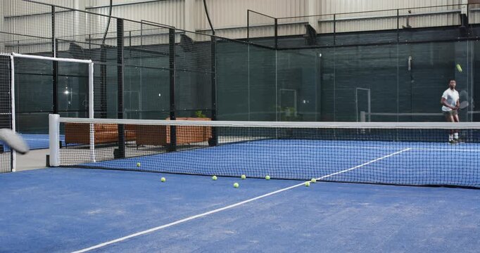 Male friends in t-shirts practicing volley at padel court, smashing overhead, returning shot