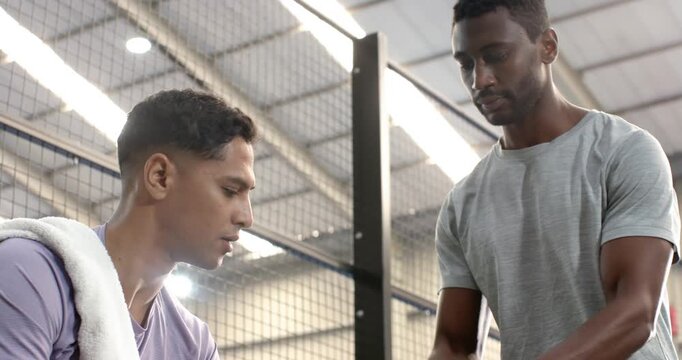 Diverse male friends receiving smartphone notification sharing juice, adjusting tracker at bench