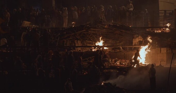 Varanasi, Uttar Pradesh, India. Cremation in process on Manikarnika Ghat. Cinematic Camera movement moving along riverbank embankment. View from riverside. night lights. Fire, smoke - Funeral rites of