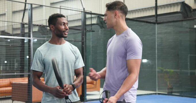 Stepping through padel net, diverse male athletes walking at court tapping rackets, sharing tips