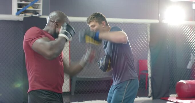 Diverse male coach and trainee on coach signal practicing focus mitt combos in cage for training