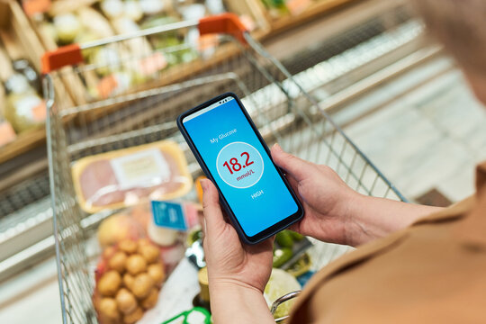 Close up of adult woman with diabetes checking high glucose on smartphone while shopping in supermarket. Useful for diabetes management, nutrition, healthcare marketing
