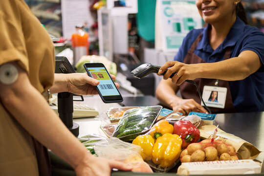 Adult woman with diabetes paying by smartphone at supermarket checkout applying store credit, glucose sensor on arm while buying groceries. Ideal for diabetes management, retail payment