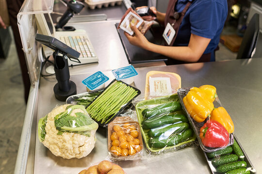 Hispanic young woman scanning groceries at supermarket checkout, showing retail service and consumer purchase concept. Ideal for grocery retail marketing