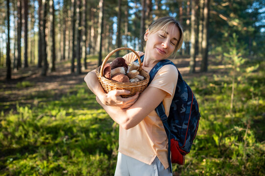 Pleased relaxed woman forager on mushroom picking in forest standing hugging basket full of porcini, happy smiling female gathering edible boletus mushrooms in woods, hobby activity and nature loving