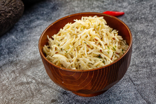 Indian cumin rice jeera rice served in wooden bowl with red chili pepper on stone table background