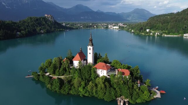 4K 30fps aerial view of Bled Island with the Assumption of Mary Church on Lake Bled, Slovenia. Beautiful cinematic footage of the iconic island surrounded by turquoise blue water and Alps mountains