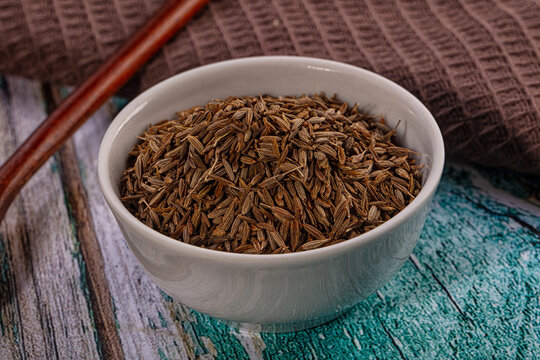 Dried cumin seeds in white ceramic bowl on rustic wooden table