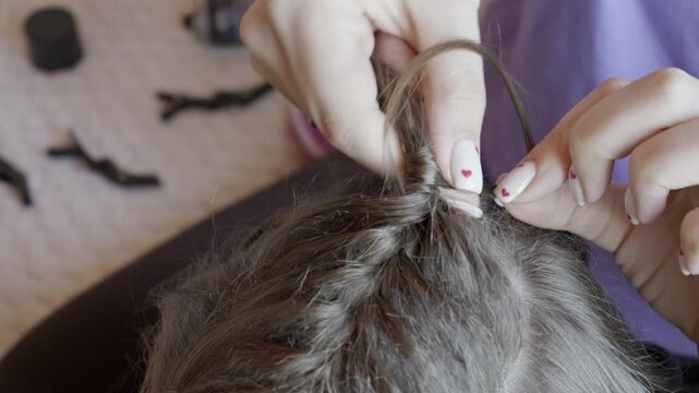 Female hands carefully wrap a thin strand of hair around a ponytail base to hide the elastic. Concept of daily personal grooming, creative hair styling, and professional beauty care.