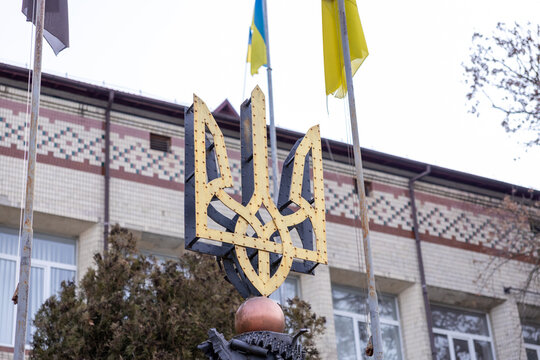Horodok, Ukraine - March 23, 2026: A golden metal Tryzub emblem stands prominently in front of an administrative building under flags, representing national identity and pride