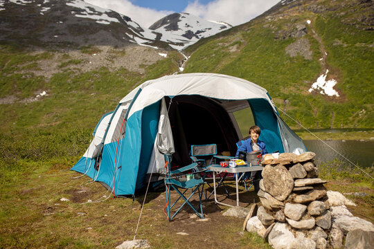 Kids, sitting in front of a piched tent in nature, enjoying wild camping. Family vacation