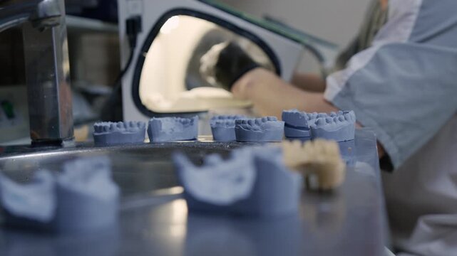 Dental technician using a sandblasting machine to process artificial jaws in a modern laboratory
