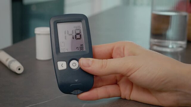 A woman swipes through her glucometer diary in the kitchen. She reviews her past blood sugar results to monitor her diabetes management.