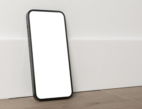 Blank smartphone mockup with green screen on a wooden floor. Angled mobile phone in a minimal interior against a white wall. Copy space for app design, advertising, and technology