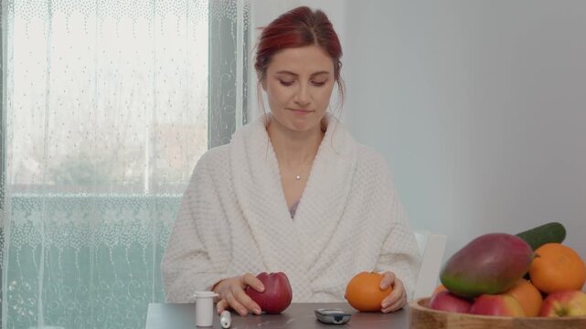 A woman in a kitchen checks her blood sugar level with a glucometer and thinks about eating an apple or an orange. Fruits are on the table along with glucose tools.