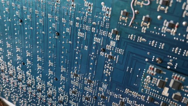 A macro view of a blue printed circuit board reveals its complex electronic components and soldered connections. Intricate traces and microchips create a landscape of modern technology.