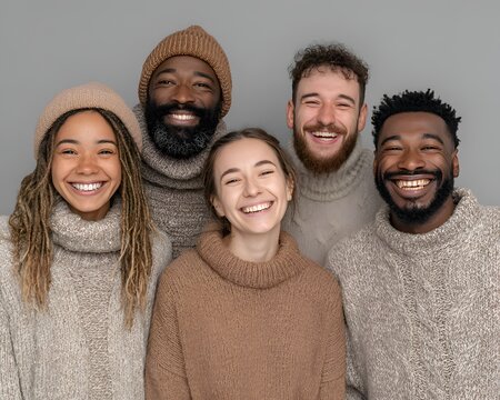 Diverse group of happy young friends in warm knitted sweaters and beanies smiling broadly