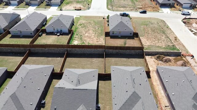 Retaining Wall Division show stone barrier separating tiered backyard plots within Highpointe Ranch. Uniform composite shingled rooftops, wooden fences, Aubrey, Dallas Fort Worth metroplex, TX