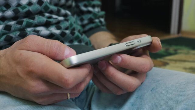 Man hands grip a silver smartphone in a horizontal orientation while sitting, highlighting active interaction with the device. Concept of mobile gaming and digital entertainment.