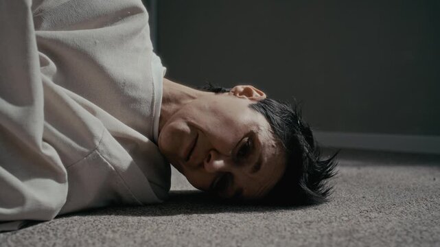 Closeup portrait of middle aged Caucasian woman lying on floor in straitjacket, breathing heavily in psychiatric clinic. Clip is suitable for mental health awareness campaigns or medical documentaries