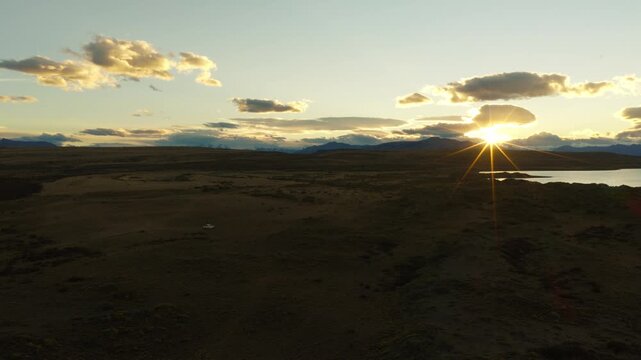 Drone tracking above Patagonian steppe near Lago Viedma and El Chalt&eacute;n, Santa Cruz, Argentina, featuring golden sunset light, glacial lake shoreline and the Fitz Roy massif beneath dramatic clouds.