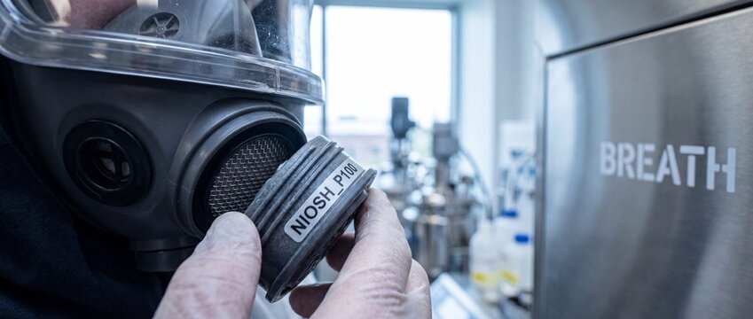 Full face respirator mask filter replaced by hand in industrial chemical laboratory for safety compliance and occupational health protection using certified P100 particulate purification cartridge.